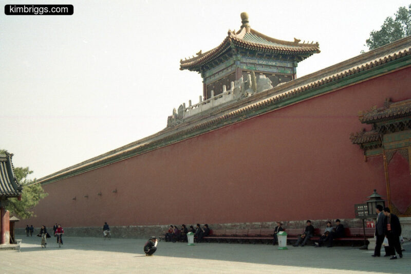 People on bench in front of Forbidden City wall.