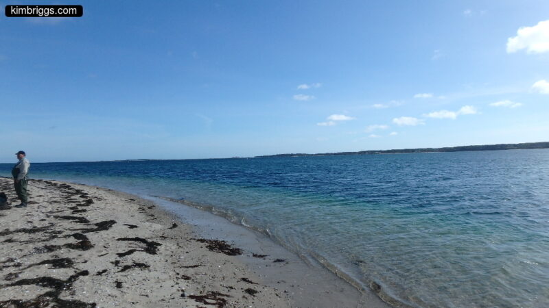 Man in fishing overalls on beach.