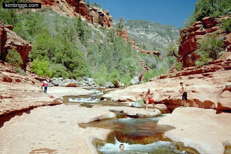 People in Slide Rock Park river with mountains in background.