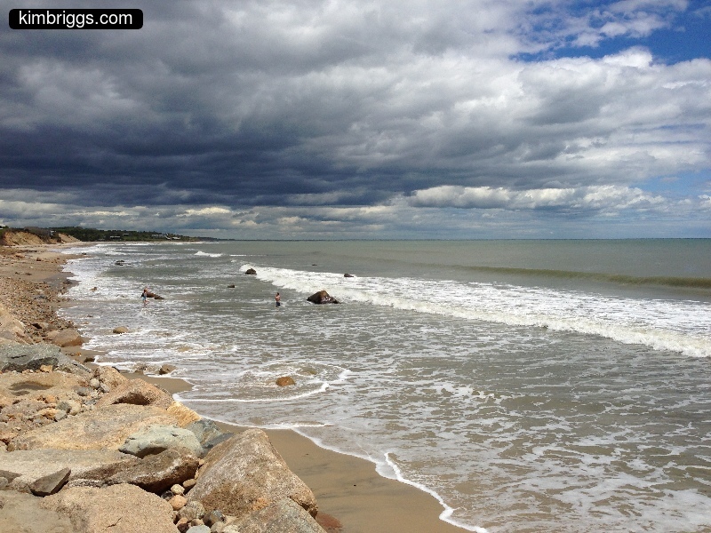 Puffy grey clouds over rocky beach.