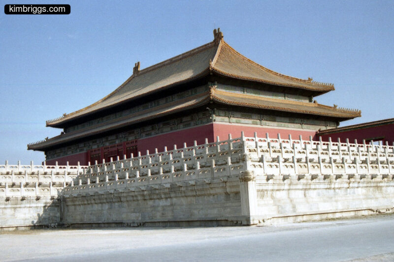 Large Chinese building with curved roof and huge stone wall in front.