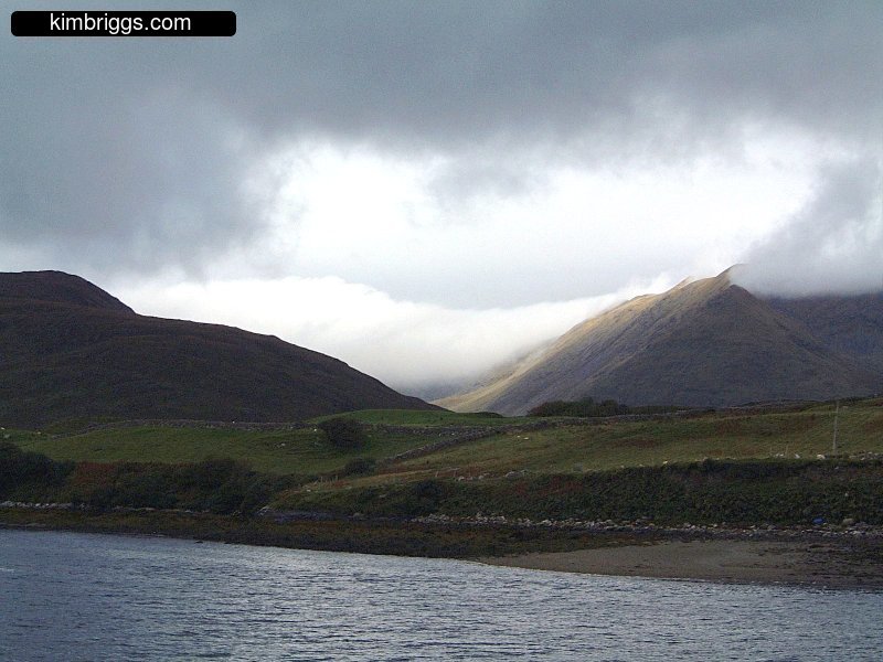 Clouds laying on green hills.