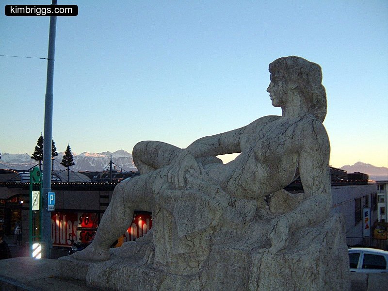 Stone statue of lounging woman outdoors.