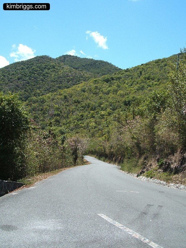 Paved road leading to small green hills.