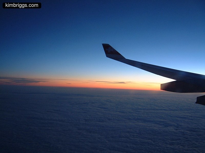 Airplane wing silhouette viewing sunrise in the sky.
