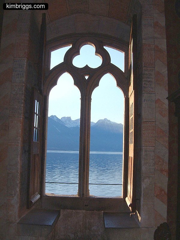 Old castle window framing lake with mountains.